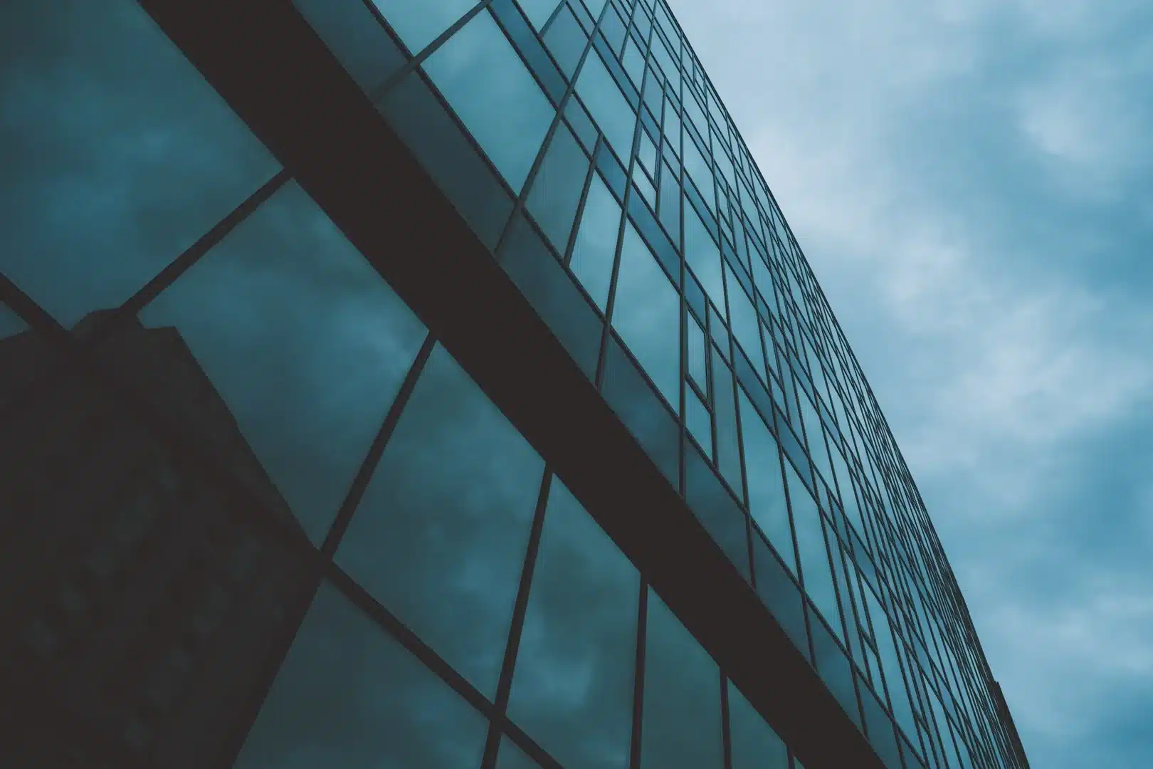 Gratte-ciel moderne aux façades en verre reflétant un ciel nuageux sous une lumière bleutée.