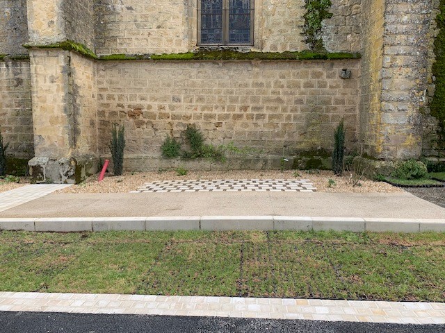 Mur en pierre ancienne et aménagement paysager avec gravier, dalles et gazon bordant un édifice historique.
