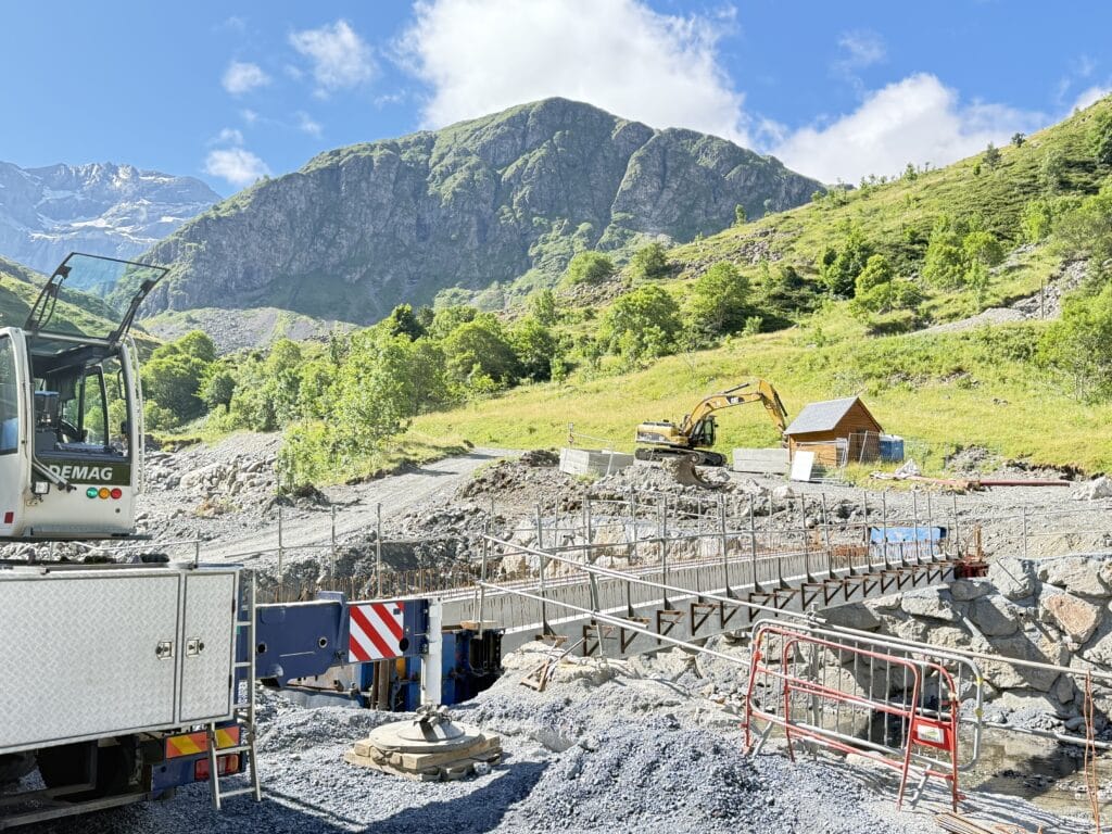 Chantier de pont en montagne avec grue Demag et excavatrice Cat sous ciel bleu.