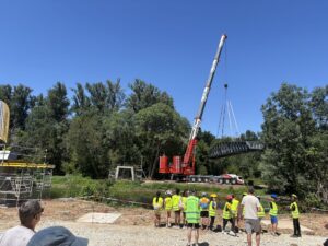 Enfants VELO-ECOLE regardant une grue lever une passerelle métallique au-dessus de l'eau.