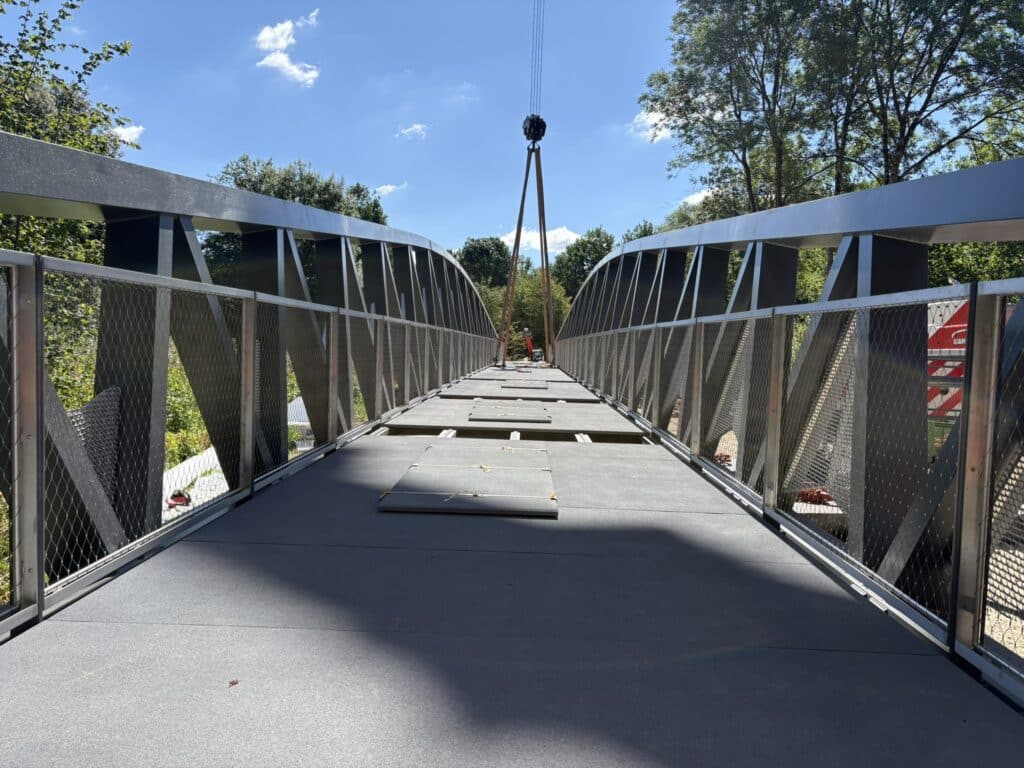 Passerelle piétonne en acier en construction avec grue sous ciel bleu dégagé.