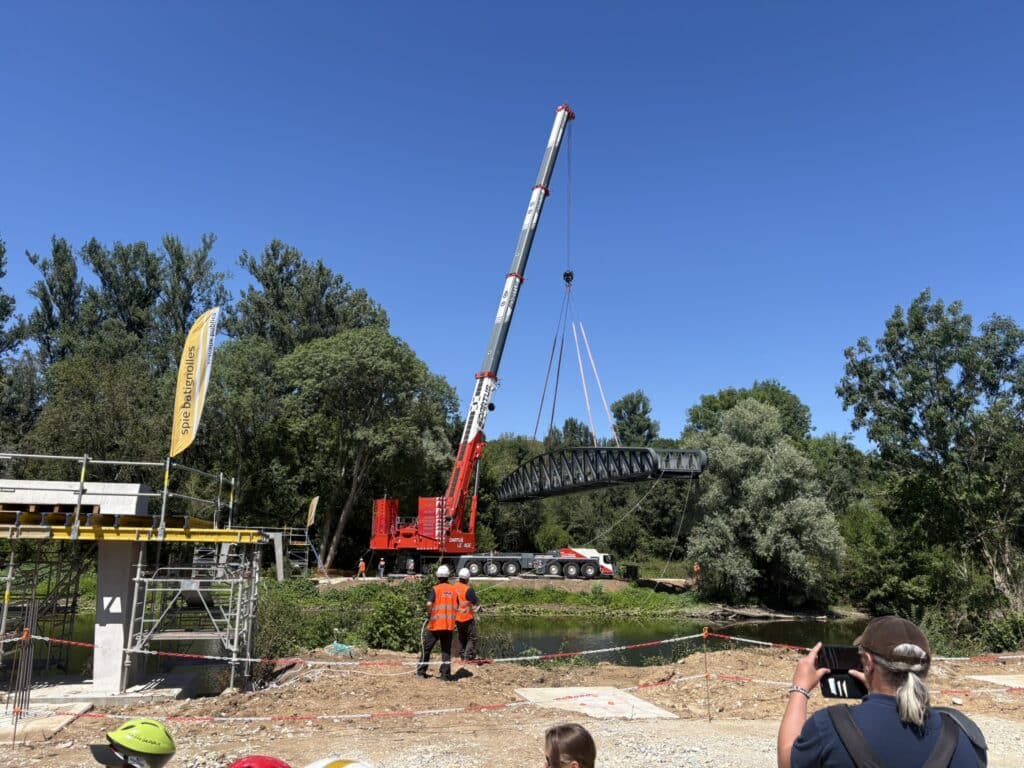 Grue Dartus levant une section de pont Spie Batignolles au-dessus d'une rivière sous un ciel bleu.