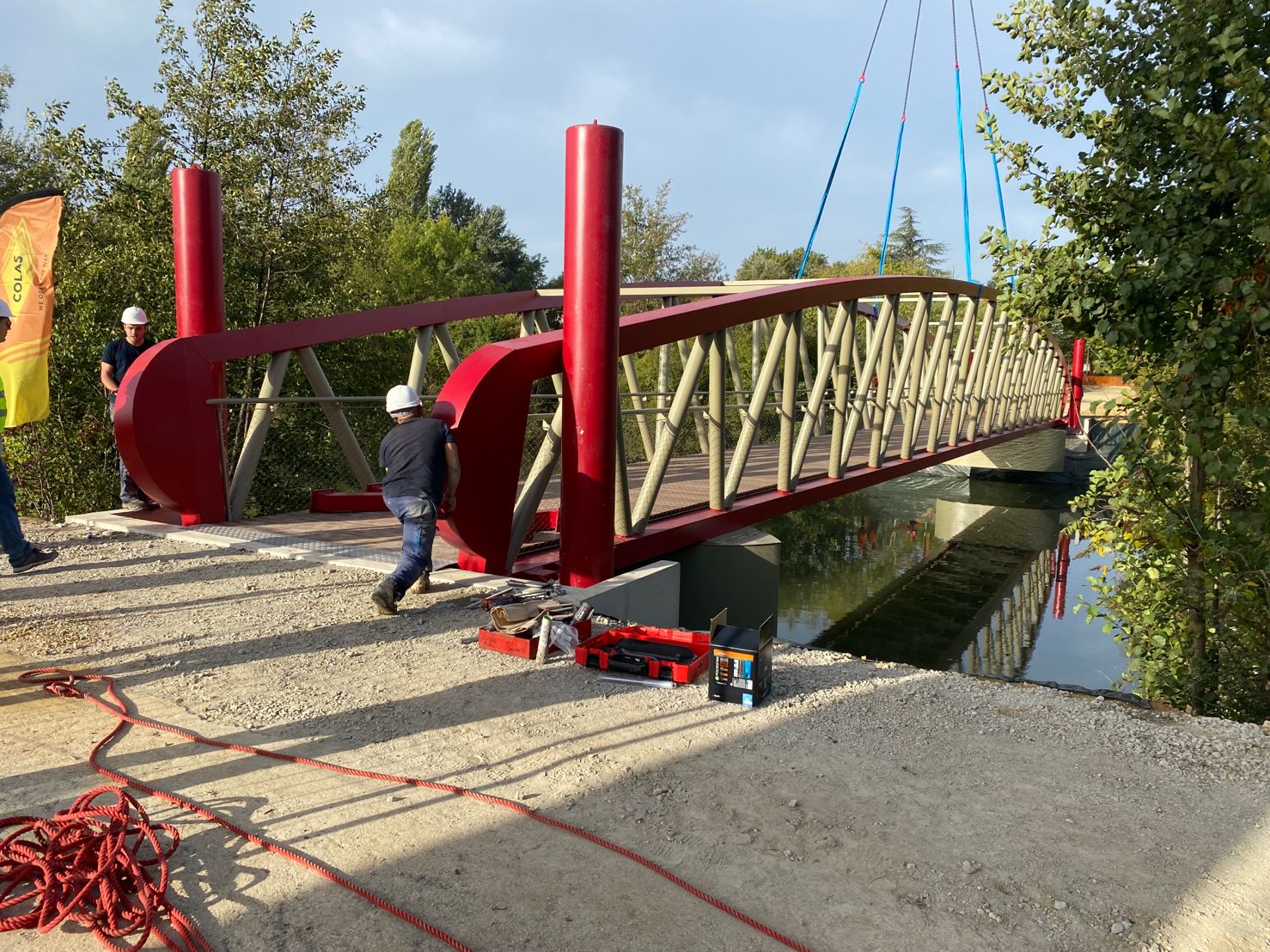 Ouvriers installant une passerelle rouge Colas au-dessus d'une rivière. Montage de structure métallique.