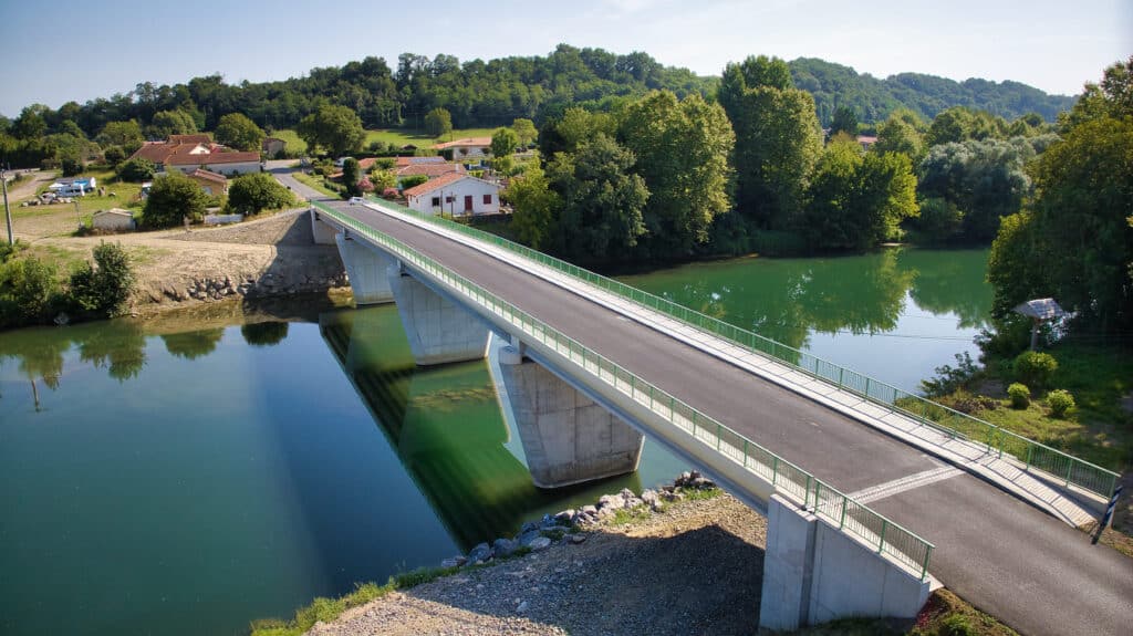 Pont moderne en béton sur une rivière calme et verdoyante Pont moderne en béton sur rivière calme, paysage rural avec maisons et collines boisées.