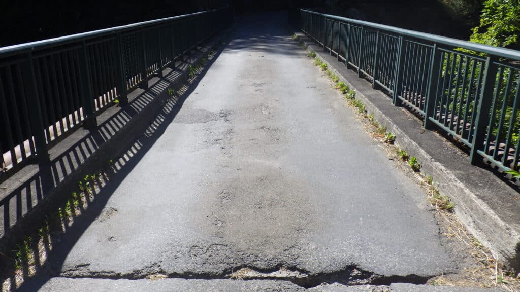 Pont en asphalte fissuré avec garde-corps métalliques et ombres portées.