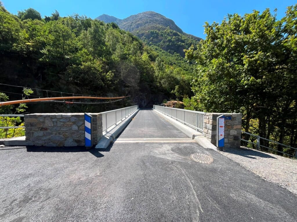 Pont moderne en montagne entouré de forêt dense sous un ciel bleu dégagé.