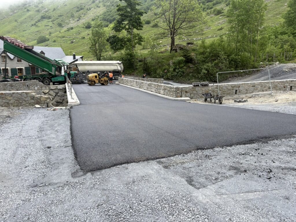 Chantier d'enrobé en montagne avec finisseur vert et rouleau compresseur jaune sur une route neuve.