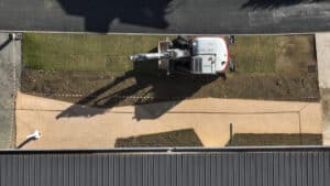 Mini-pelle sur chantier paysager : pose de gazon et aménagement de terrain, vue aérienne.